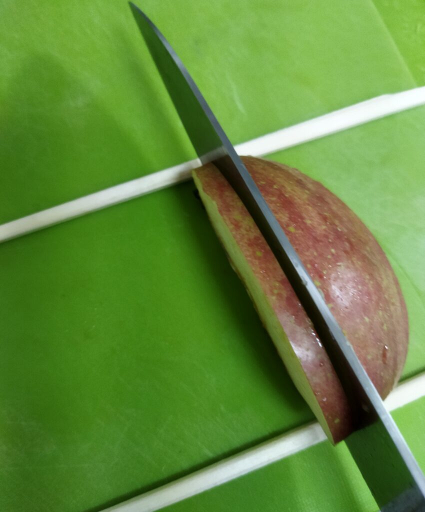 裏返してりんごの切り口から5mmくらいの厚さで、割り箸まで切り込みを入れているところ