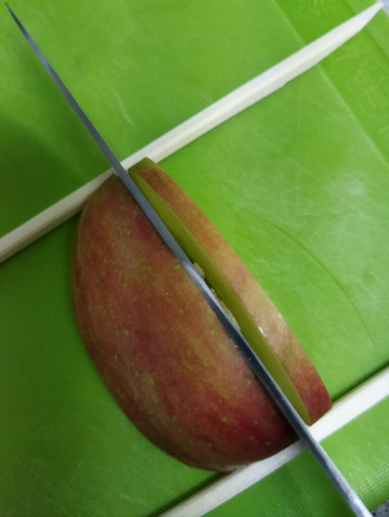 りんごの切り口から5mmくらいの厚さで、割り箸まで切り込みを入れているところ