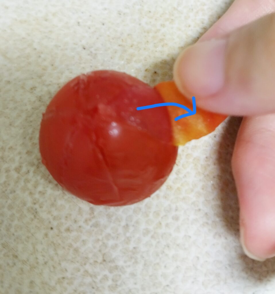 指先で、ミニトマトの中央から皮を外側にめくる様子