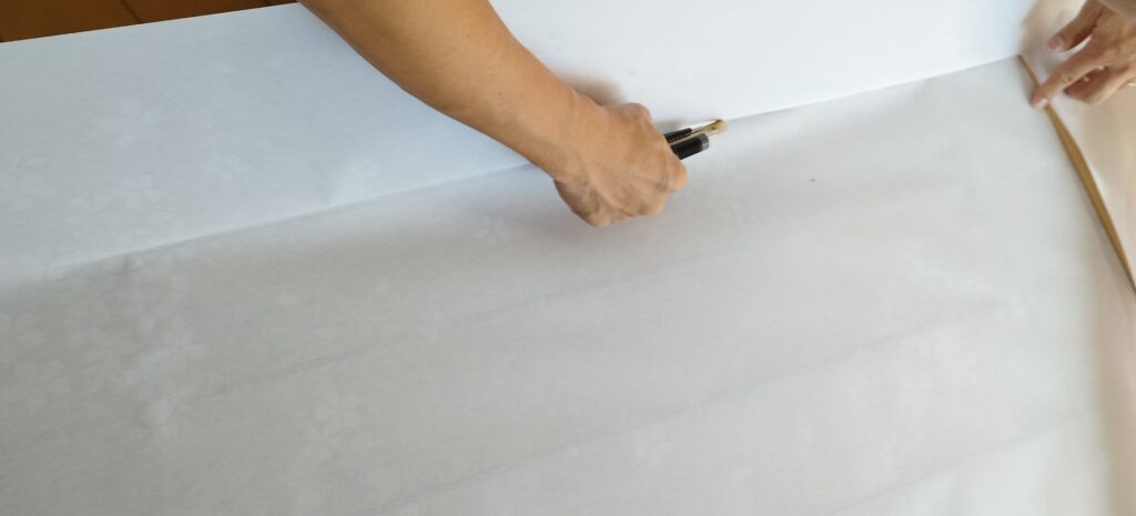 プラスチック障子紙の余分な部分をカッターで切り落とす様子